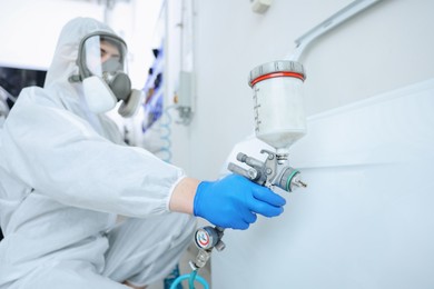 Photo of Worker painting car door in body shop, selective focus