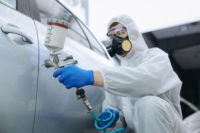 Photo of Worker painting car in body shop, selective focus