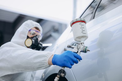 Photo of Worker painting car in body shop, selective focus