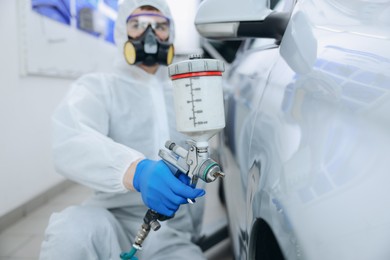 Photo of Worker painting car in body shop, selective focus