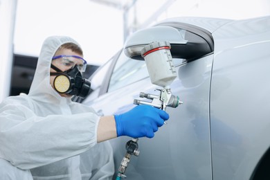 Photo of Worker painting car in body shop, selective focus