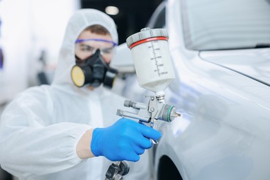Photo of Worker painting car in body shop, selective focus