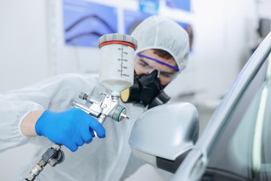 Photo of Worker painting car in body shop, selective focus