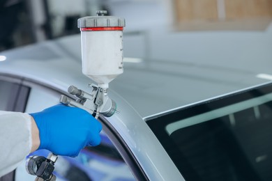 Photo of Worker painting car in body shop, closeup