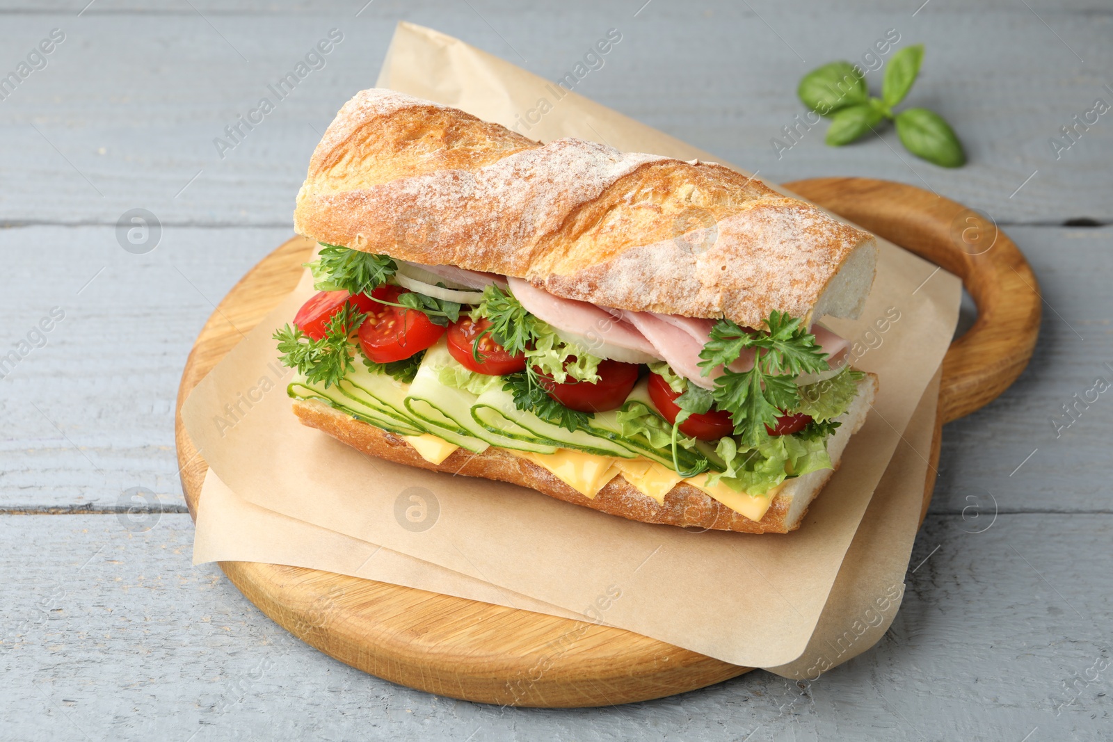 Tasty baguette sandwich with ham, cheese and vegetables on grey wooden table, closeup Photo of Tasty baguette sandwich with ham, cheese and vegetables on grey wooden table, closeup