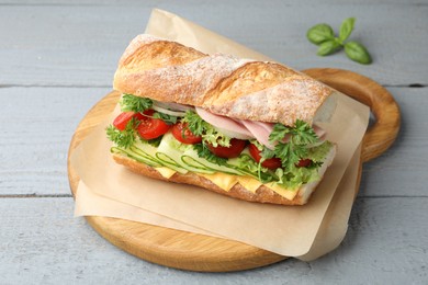 Photo of Tasty baguette sandwich with ham, cheese and vegetables on grey wooden table, closeup
