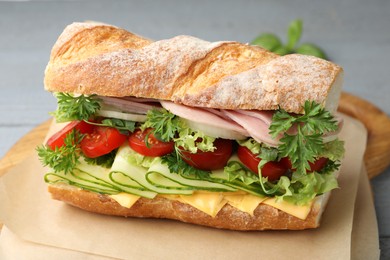 Photo of Tasty baguette sandwich with ham, cheese and vegetables on grey table, closeup