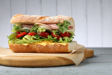 Photo of Tasty baguette sandwich with ham, cheese and vegetables on wooden table against grey background, closeup