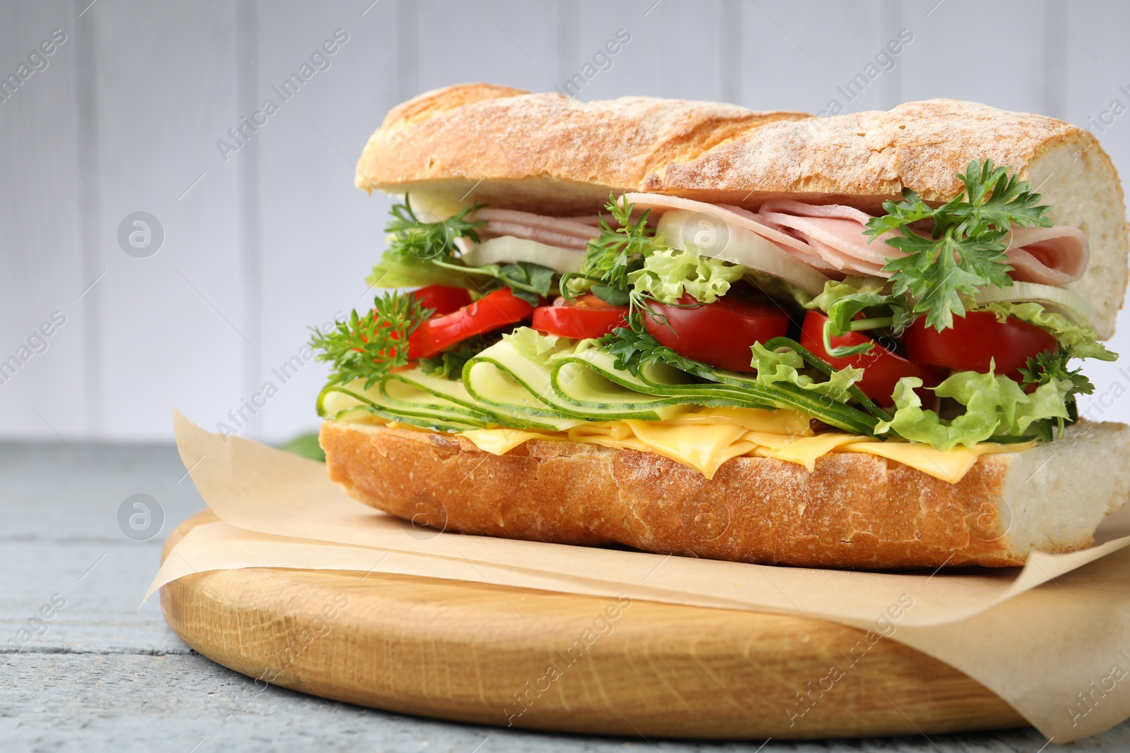 Tasty baguette sandwich with ham, cheese and vegetables on wooden table against grey background, closeup Photo of Tasty baguette sandwich with ham, cheese and vegetables on wooden table against grey background, closeup
