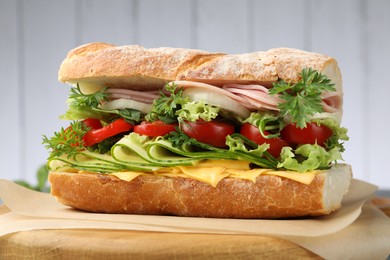 Photo of Tasty baguette sandwich with ham, cheese and vegetables on blurred grey background, closeup