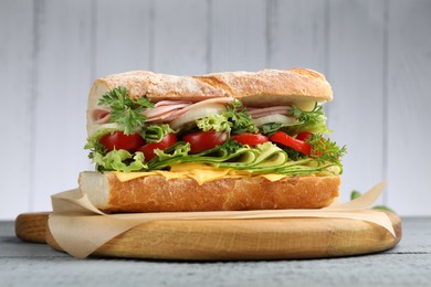 Photo of Tasty baguette sandwich with ham, cheese and vegetables on grey wooden table, closeup
