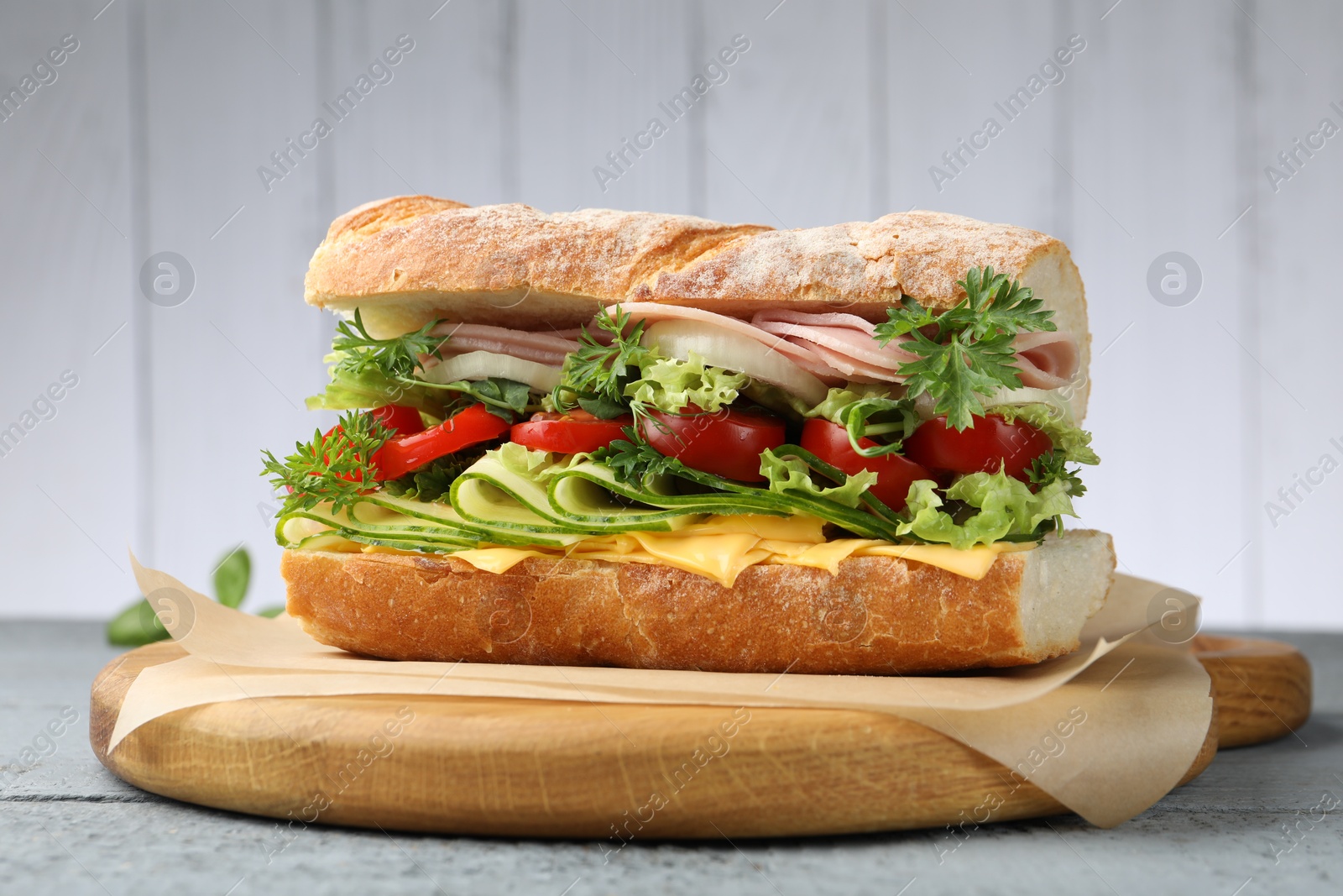 Tasty baguette sandwich with ham, cheese and vegetables on grey wooden table, closeup Photo of Tasty baguette sandwich with ham, cheese and vegetables on grey wooden table, closeup