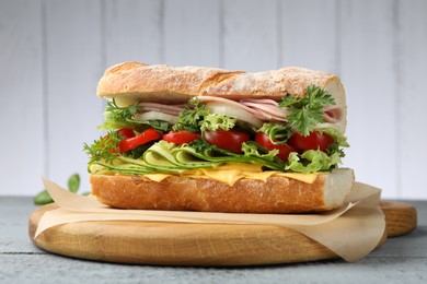 Photo of Tasty baguette sandwich with ham, cheese and vegetables on grey wooden table, closeup