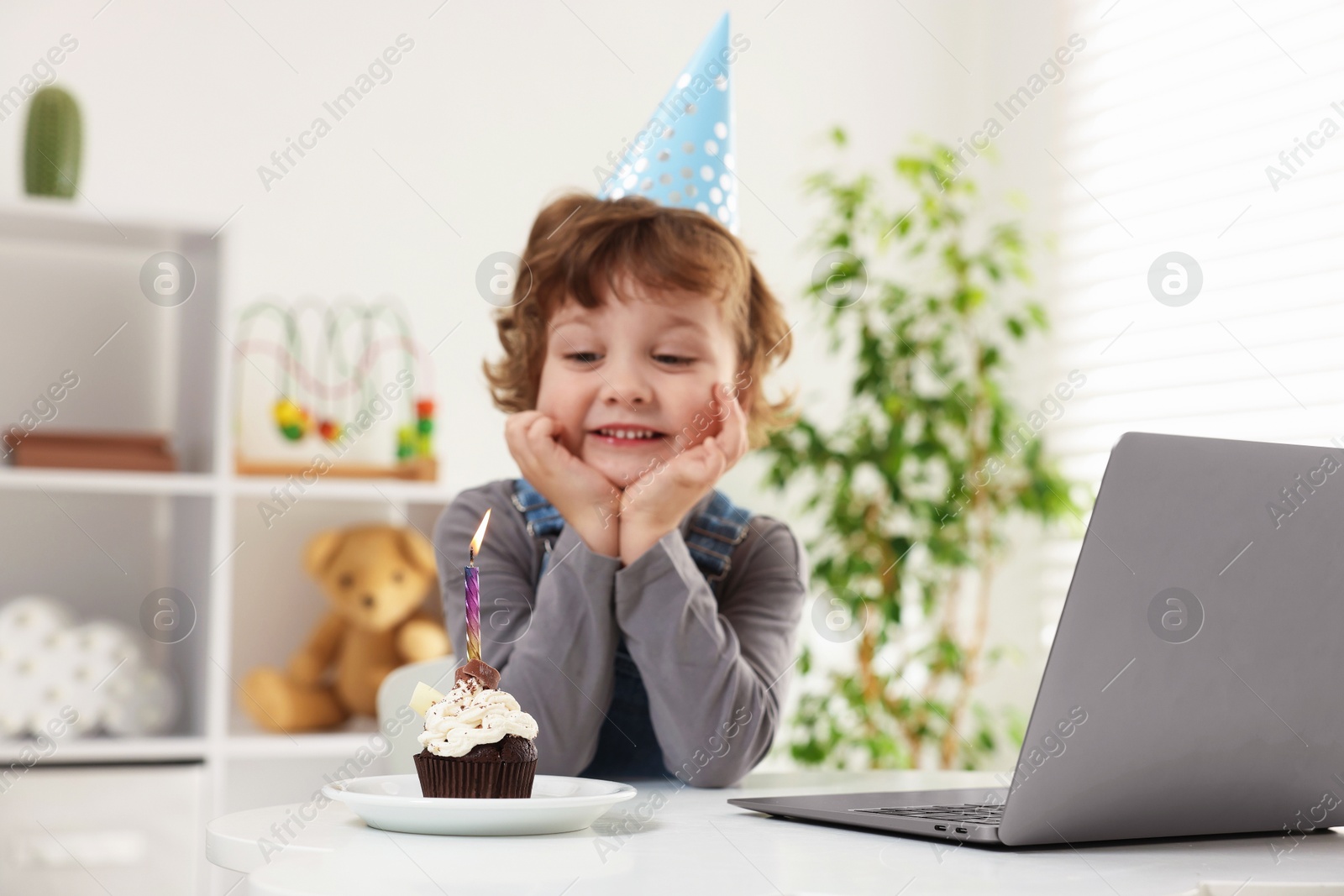Birthday celebration. Little boy with cupcake having video call via laptop at table indoors Photo of Birthday celebration. Little boy with cupcake having video call via laptop at table indoors