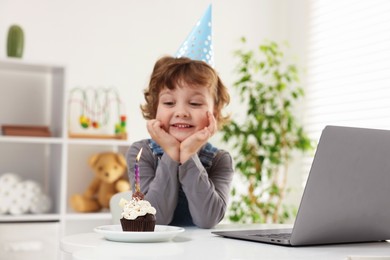 Photo of Birthday celebration. Little boy with cupcake having video call via laptop at table indoors