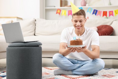 Photo of Man with cake celebrating his birthday and having video call via laptop at home