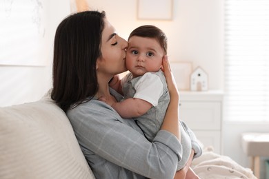 Photo of Mother kissing her cute baby on sofa at home