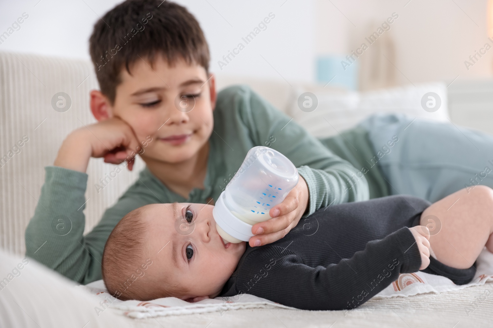 Little boy feeding his newborn brother with bottle on sofa at home Photo of Little boy feeding his newborn brother with bottle on sofa at home