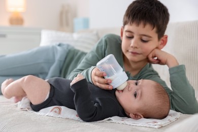 Photo of Little boy feeding his newborn brother with bottle on sofa at home