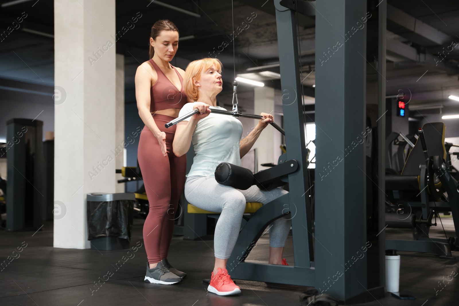 Senior woman training on lat pulldown machine supervised by professional trainer in gym Photo of Senior woman training on lat pulldown machine supervised by professional trainer in gym