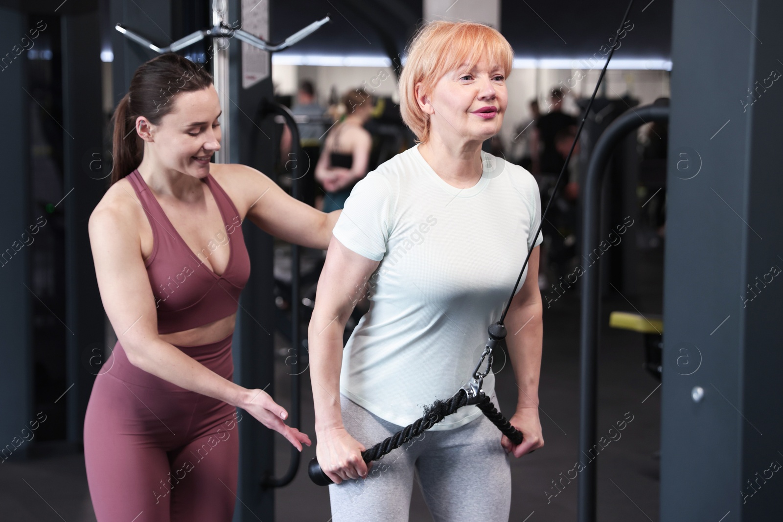Senior woman training on pulley machine supervised by professional trainer in gym Photo of Senior woman training on pulley machine supervised by professional trainer in gym