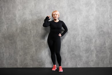 Photo of Senior woman with kettlebell near gray marble wall indoors