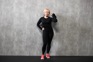 Photo of Senior woman with kettlebell near gray marble wall indoors