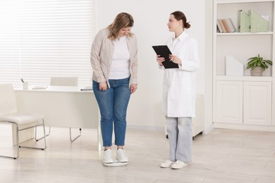 Photo of Weight loss. Overweight woman standing on scales during consultation with nutritionist in clinic