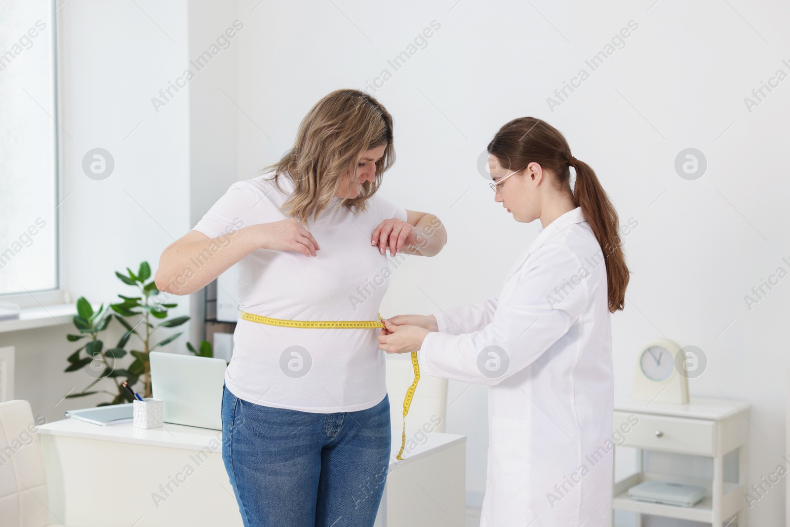 Weight loss. Nutritionist measuring overweight woman's waist with tape in clinic Photo of Weight loss. Nutritionist measuring overweight woman's waist with tape in clinic