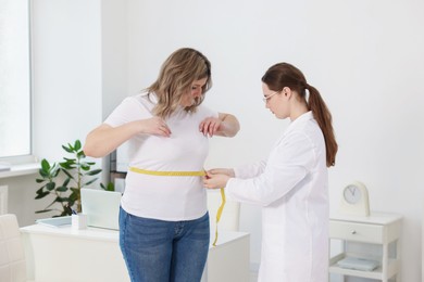 Photo of Weight loss. Nutritionist measuring overweight woman's waist with tape in clinic