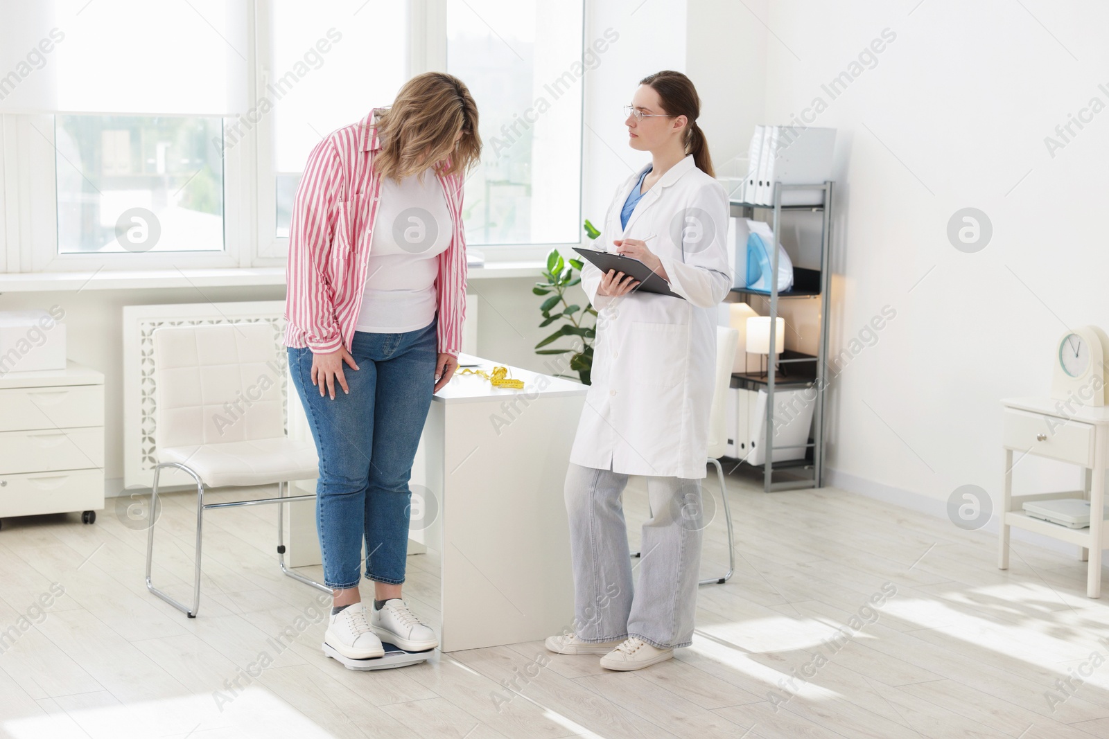 Weight loss. Overweight woman standing on scales during consultation with nutritionist in clinic Photo of Weight loss. Overweight woman standing on scales during consultation with nutritionist in clinic