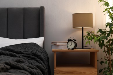 Photo of Bedside table with lamp, alarm clock and books near bed indoors. Interior design