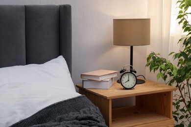 Photo of Bedside table with lamp, alarm clock and books near bed indoors. Interior design