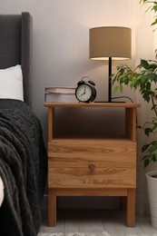 Photo of Bedside table with lamp, alarm clock and books near bed indoors. Interior design