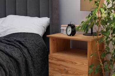 Photo of Bedside table with lamp, alarm clock and books near bed indoors. Interior design