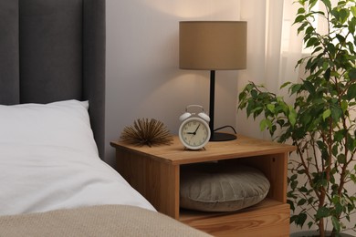 Photo of Bedside table with lamp, alarm clock and decor near bed indoors. Interior design