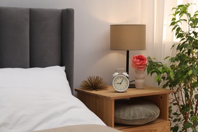 Photo of Bedside table with lamp, alarm clock and decor near bed indoors. Interior design