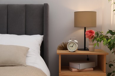 Photo of Bedside table with lamp, alarm clock, books and decor near bed indoors. Interior design