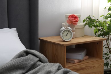 Photo of Bedside table with alarm clock, books and decor near bed indoors. Interior design