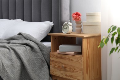 Photo of Bedside table with alarm clock, books and decor near bed indoors. Interior design