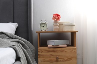 Photo of Bedside table with alarm clock, books and decor near bed indoors. Interior design
