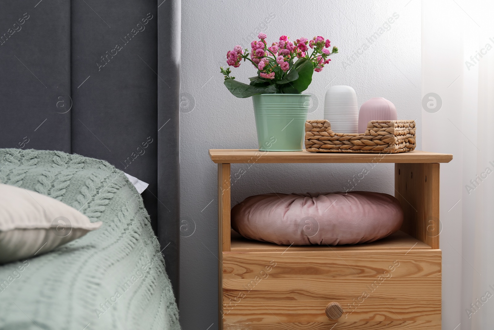 Bedside table with flowers and decor near bed indoors Photo of Bedside table with flowers and decor near bed indoors