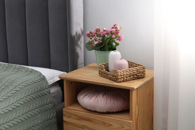 Photo of Bedside table with flowers and decor near bed indoors