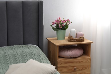 Photo of Bedside table with flowers and decor near bed indoors