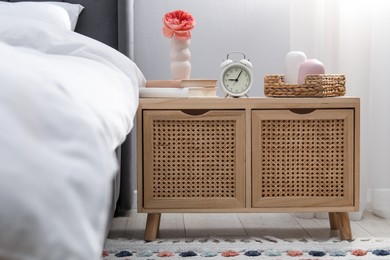 Photo of Bedside table with alarm clock and decor near bed indoors