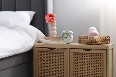 Photo of Bedside table with alarm clock and decor near bed indoors