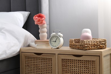 Photo of Bedside table with alarm clock and decor near bed indoors