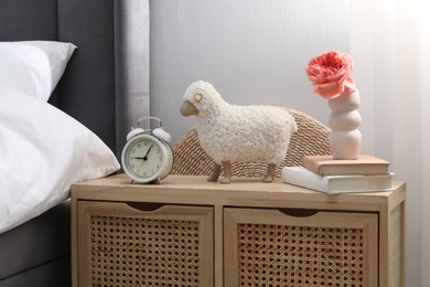 Photo of Bedside table with alarm clock, decor and books near bed indoors