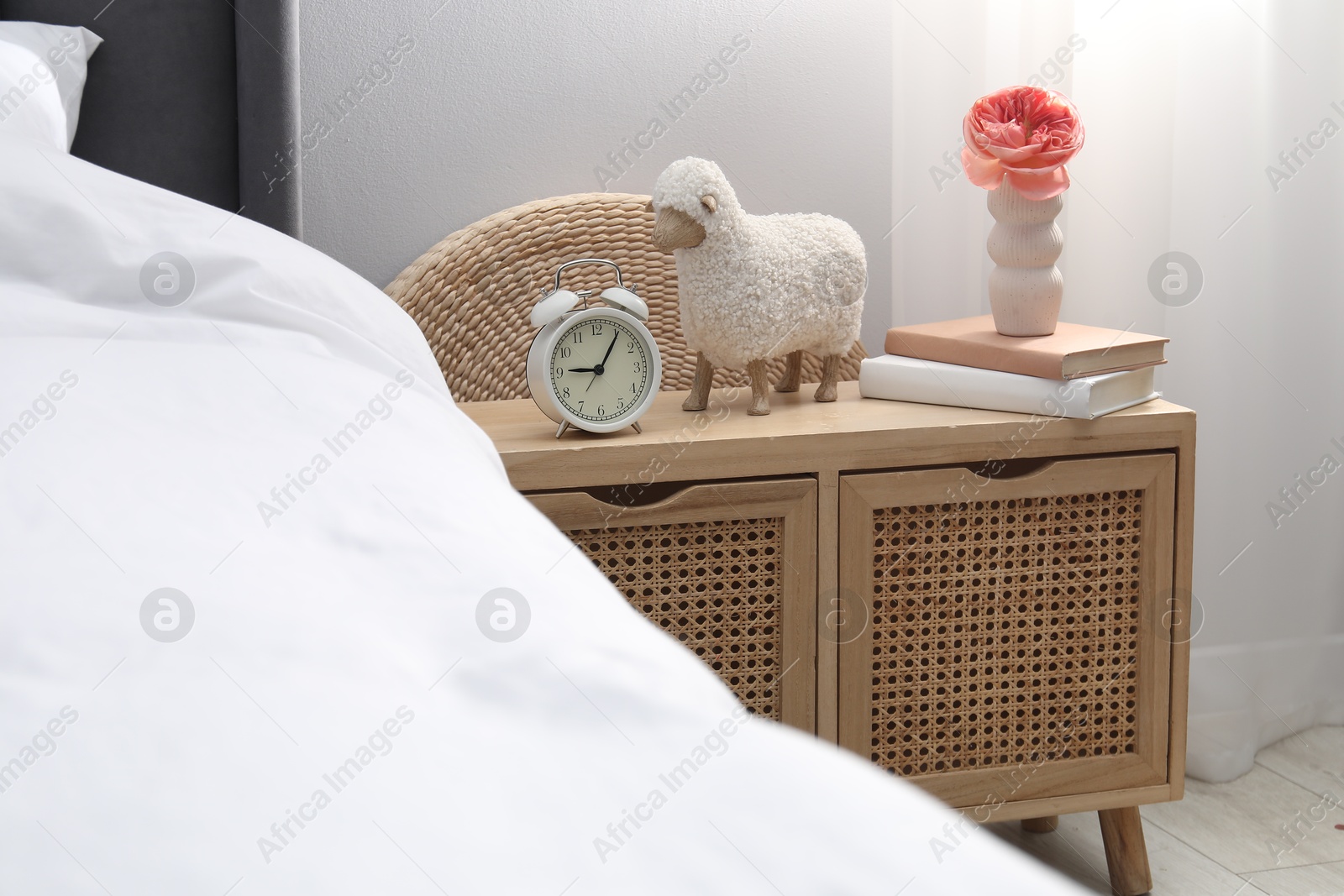 Bedside table with alarm clock, decor and books near bed indoors Photo of Bedside table with alarm clock, decor and books near bed indoors