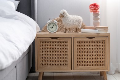 Photo of Bedside table with alarm clock, decor and books near bed indoors